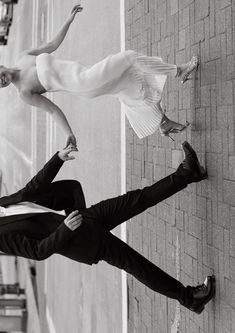 black and white photograph of two people leaning against a wall with their arms in the air