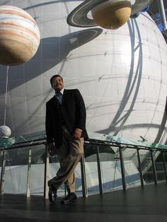 a man in a suit and tie standing next to a large white ball with saturn on it