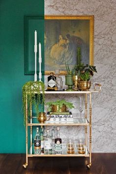 a shelf with plants, candles and bottles on it in front of a wall painting