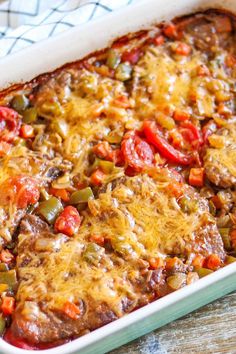 a casserole dish with meat, cheese and peppers in it on a wooden table