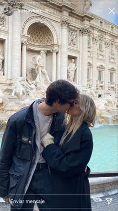 a man and woman kissing in front of a fountain