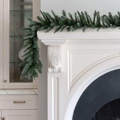 a white fireplace with a green garland on it's mantle next to a glass cabinet