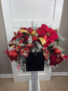 a christmas wreath with poinsettis and greenery on a black box in front of a white door