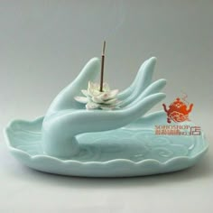 a white flower floating on top of a blue plate with incense sticks in the middle