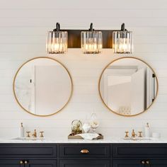 two round mirrors are above the double sink vanity in this white and black bathroom with gold accents