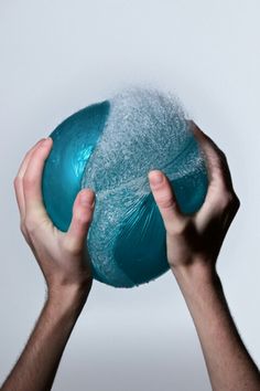 two hands are holding a blue ball with white powder on it, against a gray background