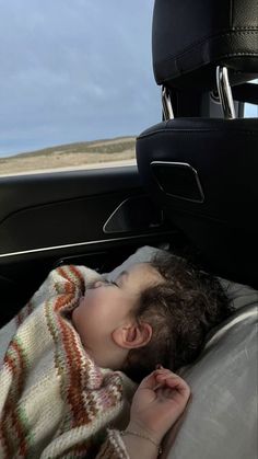 a small child sleeping in the back seat of a car with a blanket on it