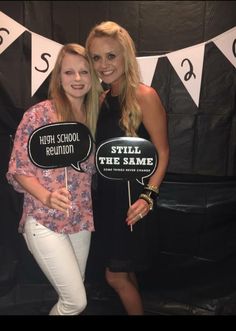 two women standing next to each other in front of a black and white backdrop holding signs