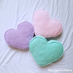 three crocheted heart shaped cushions on a bed