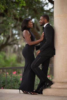 a man and woman standing next to each other in front of a pillar with trees