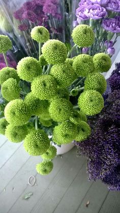 purple and green flowers in a white vase on a wooden floor next to each other