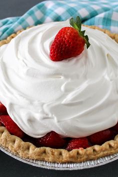 a close up of a pie with whipped cream and a strawberry on top, sitting on a blue checkered cloth