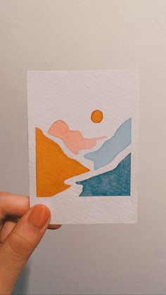 a person holding up a piece of paper with mountains and sun in the background on it