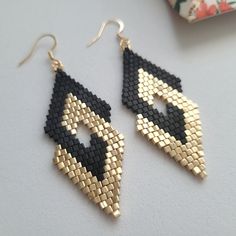 two pairs of black and gold beaded earrings on top of a white table next to a flower