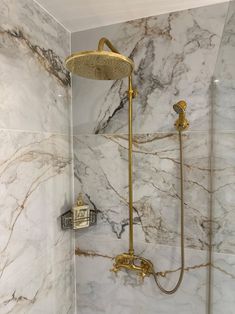 the shower head is gold in color with marble walls and flooring, along with a brass faucet