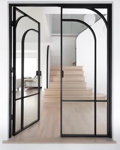 an open door leading to a staircase in a white room with wood floors and glass doors