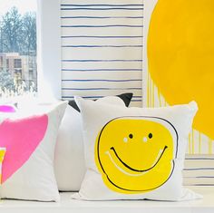 three pillows with smiley faces on them are sitting on a white shelf in front of a window