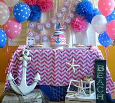 a table with pink, blue and white decorations on it next to balloons in the shape of an anchor