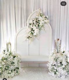 white flowers and greenery are arranged in front of the headboard for a wedding ceremony