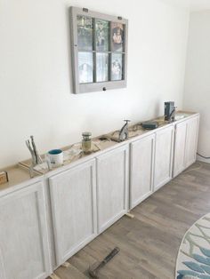 a kitchen with white cabinets and drawers under a window next to a rug on the floor