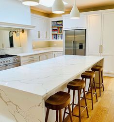 a large kitchen with white cabinets and marble counter tops, three stools are in front of the island