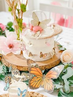 a table topped with a white cake and lots of butterflies on top of it next to flowers