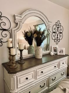 a white dresser topped with a mirror and vase filled with flowers on top of it