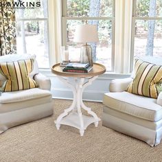 a living room with two chairs and a table in front of a window that has books on it