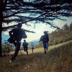 four people are running up a hill in the grass with trees and mountains behind them