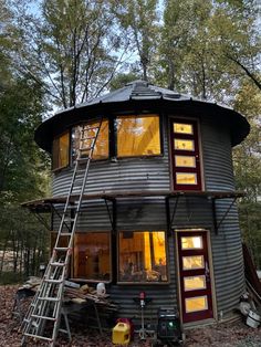 a small round house in the woods with stairs leading up to it's second floor