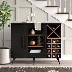 a black cabinet with wine bottles and glasses on it next to a stair case that has a potted plant in it