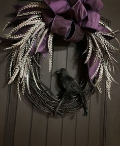 a black bird sitting on top of a grape colored wreath with purple ribbon hanging from it's front door