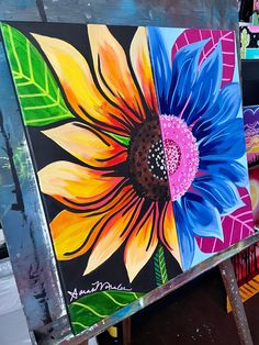 an easel with some paintings on it in front of other items and one has a sunflower painted on it