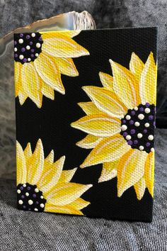 a black and yellow painted wallet with sunflowers on the front, sitting on a gray background