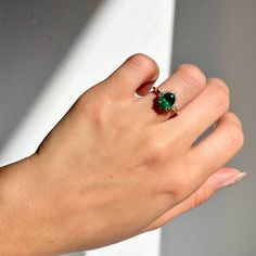 a woman's hand wearing a ring with a green stone in the middle and a white background