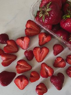 some strawberries are laying on the counter next to a bowl of strawberries and one is cut in half