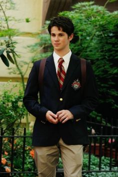 a young man wearing a suit and tie standing in front of a black iron fence