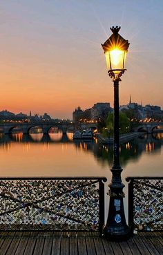 a street light sitting on the side of a wooden walkway next to a river at sunset