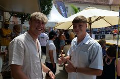 two men standing next to each other in front of umbrellas at an outdoor event