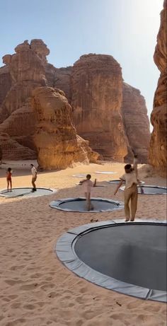 some people are playing frisbee in the sand near rocks and cliffs on a sunny day