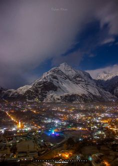 the city lights are lit up at night in front of snow - capped mountain peaks