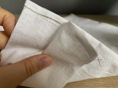 someone is sewing something on a piece of white fabric with their thumbnails out