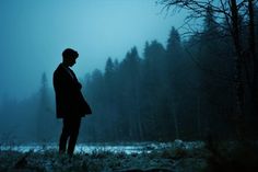 a man standing in the woods at night with his back to the camera, looking down