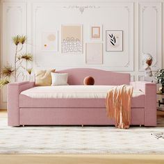 a living room with a pink couch and pillows on the floor, in front of a white wall