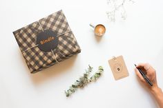 a person writing on a piece of paper next to a present box and coffee cup