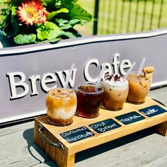 three different types of drinks sitting on a wooden table next to a sign that says brew cafe