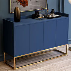 a blue sideboard with gold legs and a painting on the wall in front of it