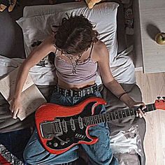 a person laying on a bed with a guitar in their hand and some books next to them