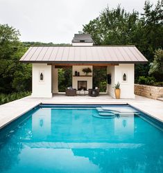 a swimming pool with a covered patio and lounge area next to it, surrounded by trees