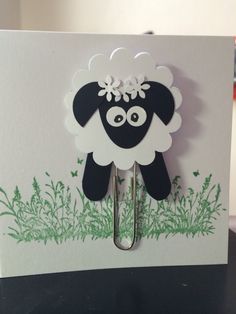 a black and white sheep with flowers on it's head is hanging from a paper clip